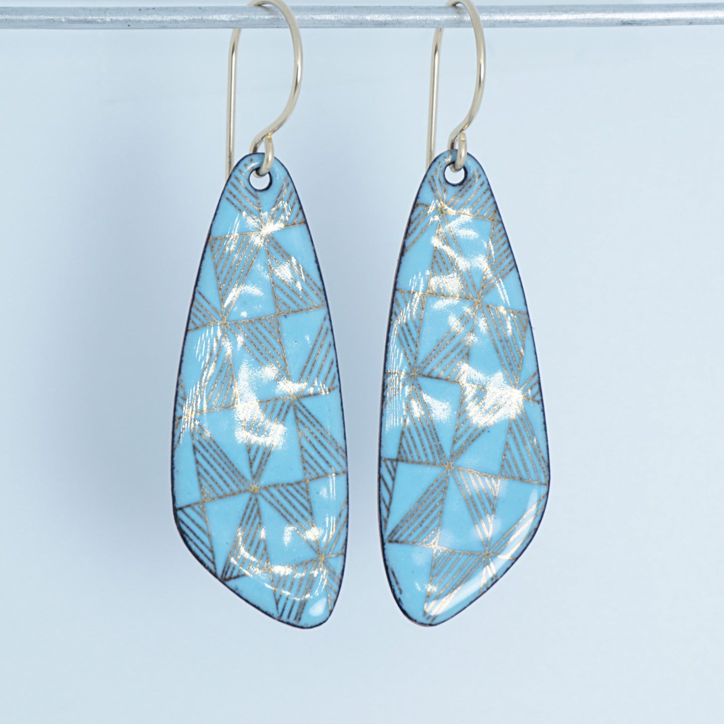 A pair of light blue enamel teardrop earrings with gold windmill print on a white background