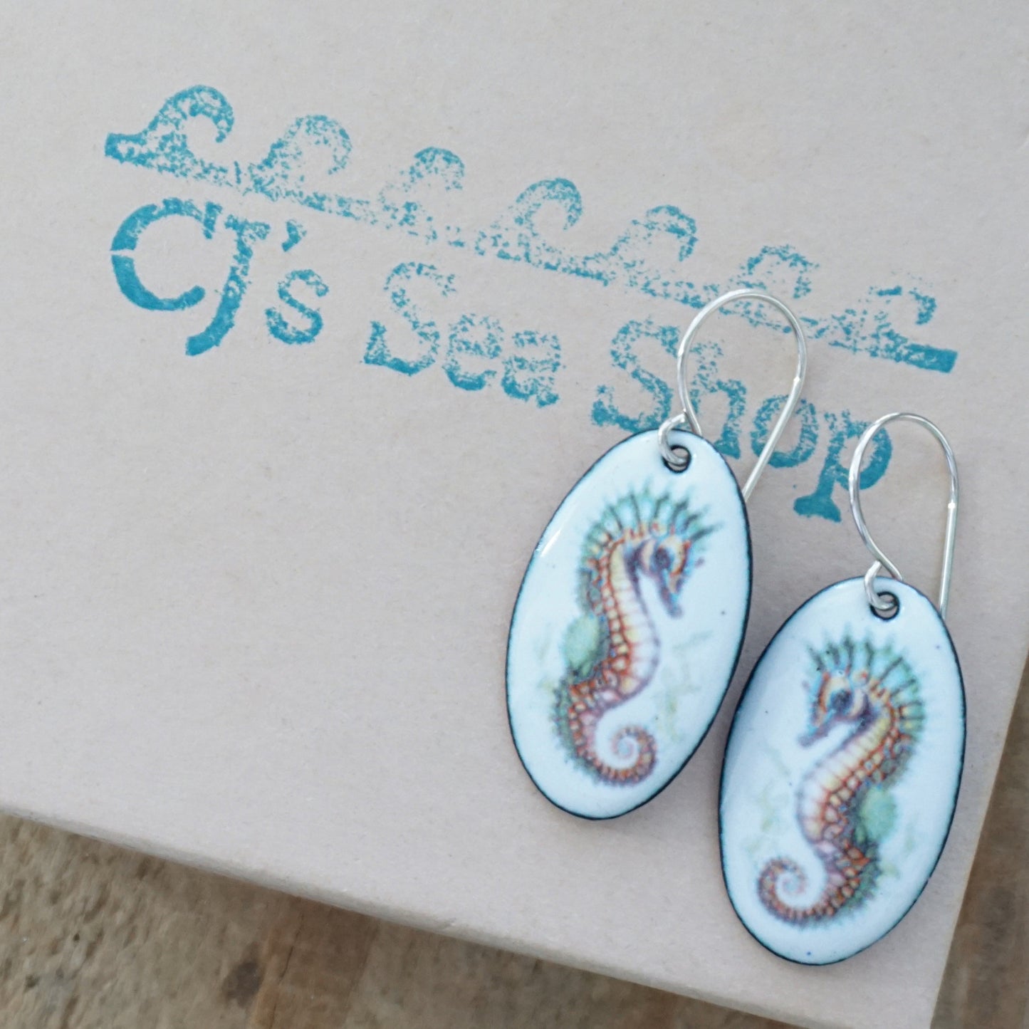 Oval earrings with seahorse design on a gift box