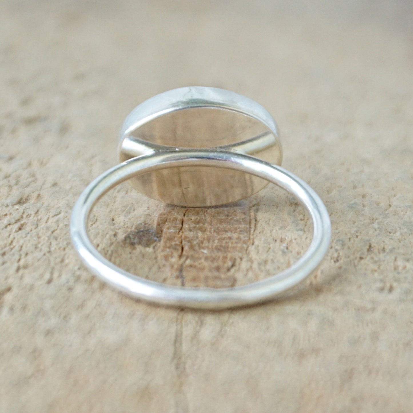 back view of a silver ring with a translucent stone on a wooden background