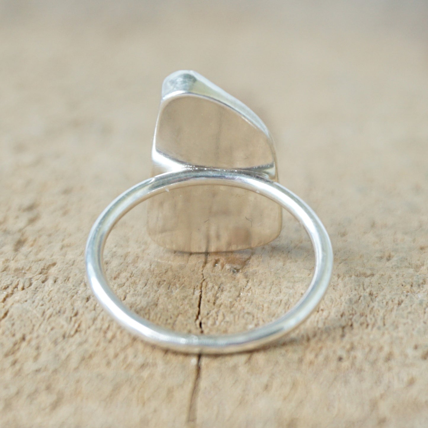 back view of a silver ring with blue sea glass on a wooden background