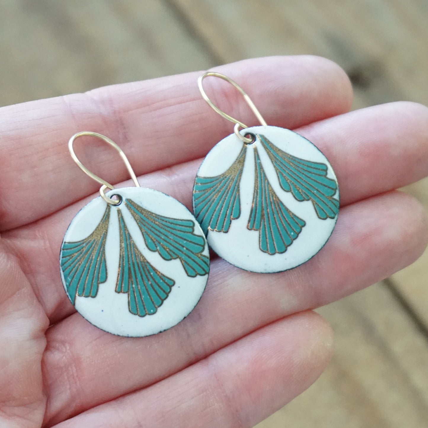 Earrings with green and gold design held in a hand against a wooden background