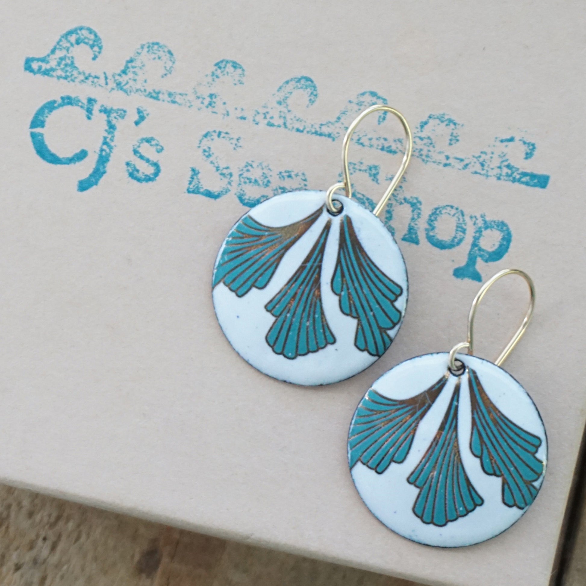 Pair of white earrings with green and gold leaf design on a gift box