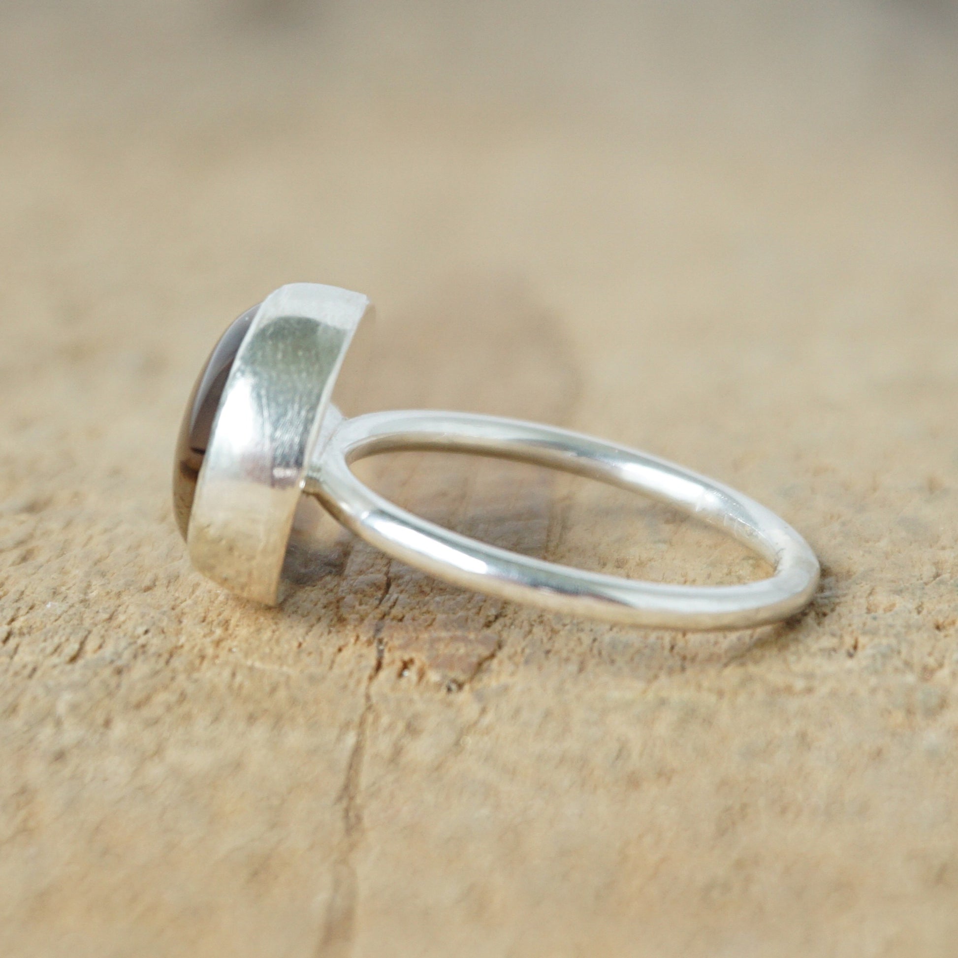 side view of a silver ring with a brown stone on a wooden background