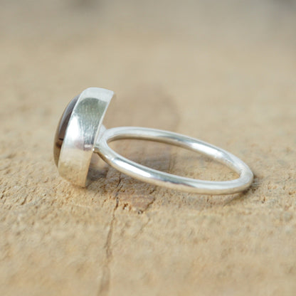 side view of a silver ring with a brown stone on a wooden background