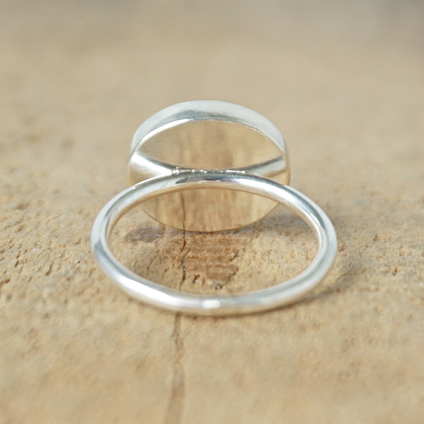 back view of a silver ring with a brown stone on a wooden background