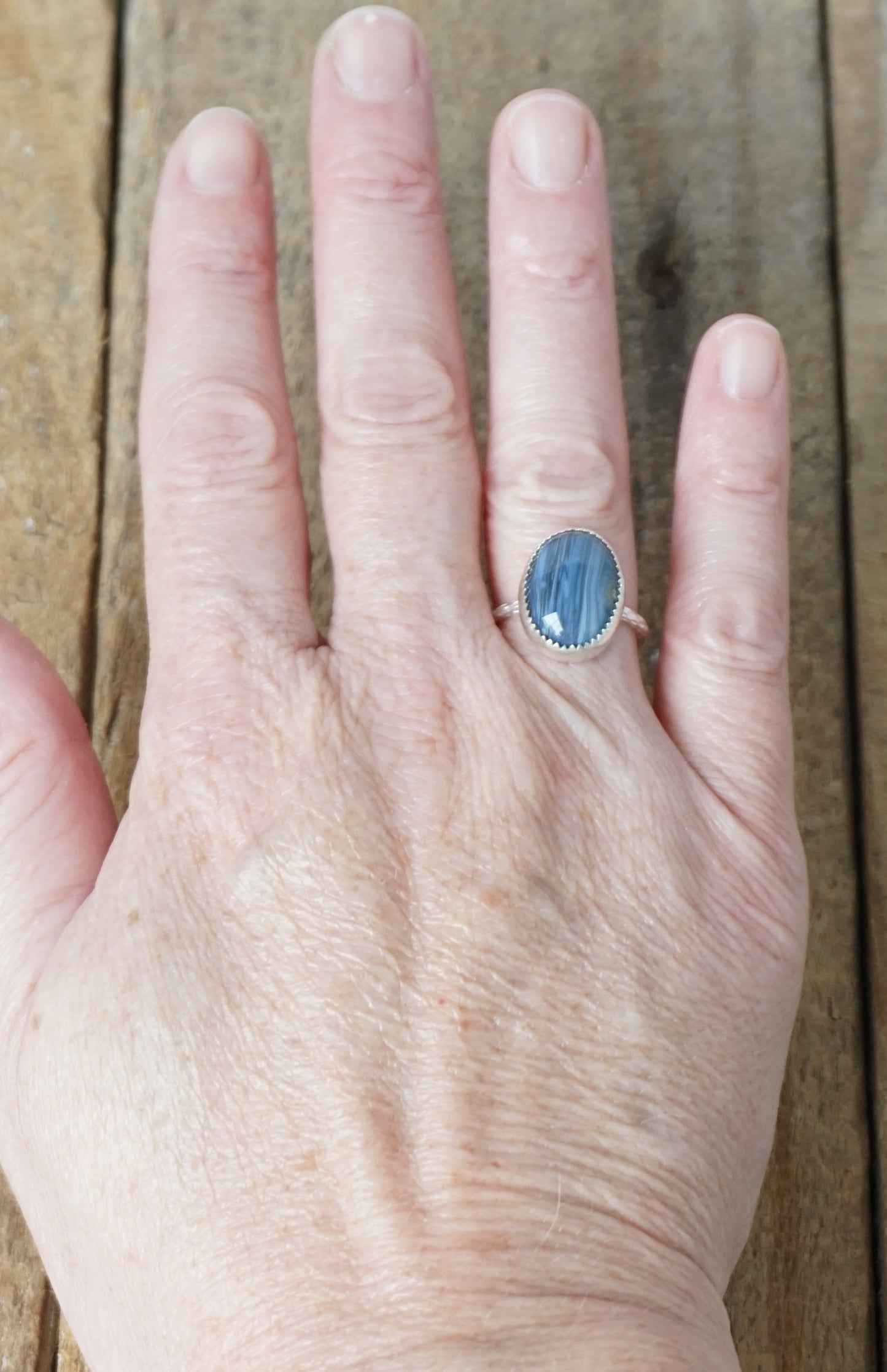 Hand wearing a ring with a blue stone on a wooden background