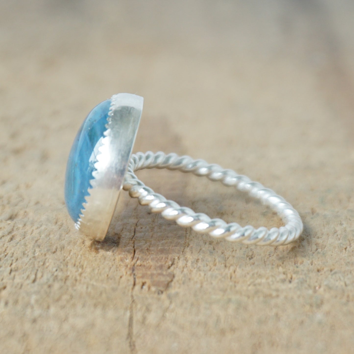 side view of a silver ring with a blue stone on a wooden background