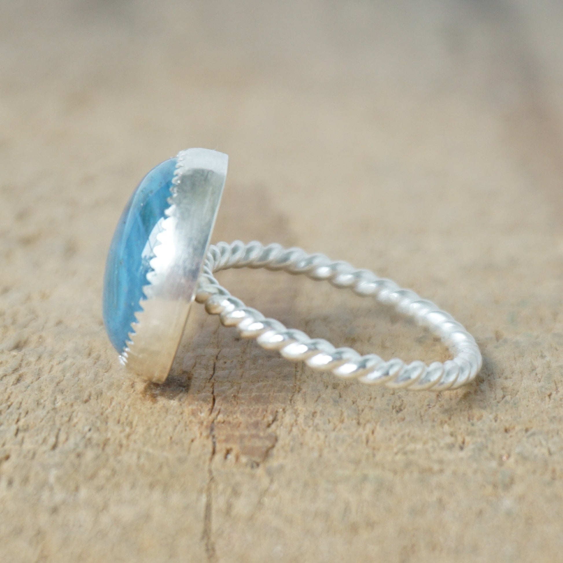side view of a silver ring with a blue stone on a wooden background