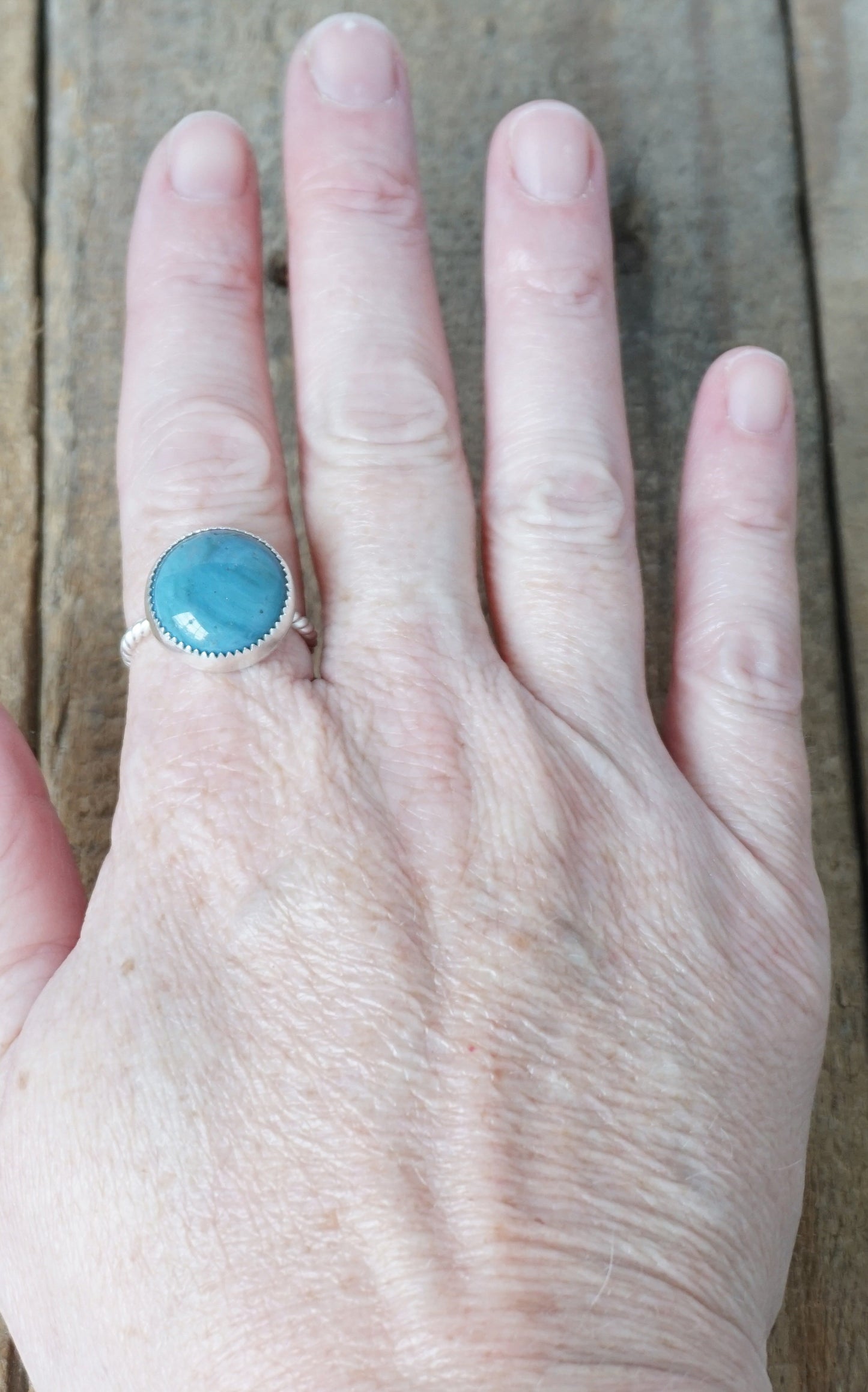 hand wearing a silver ring with a blue stone on a wooden background