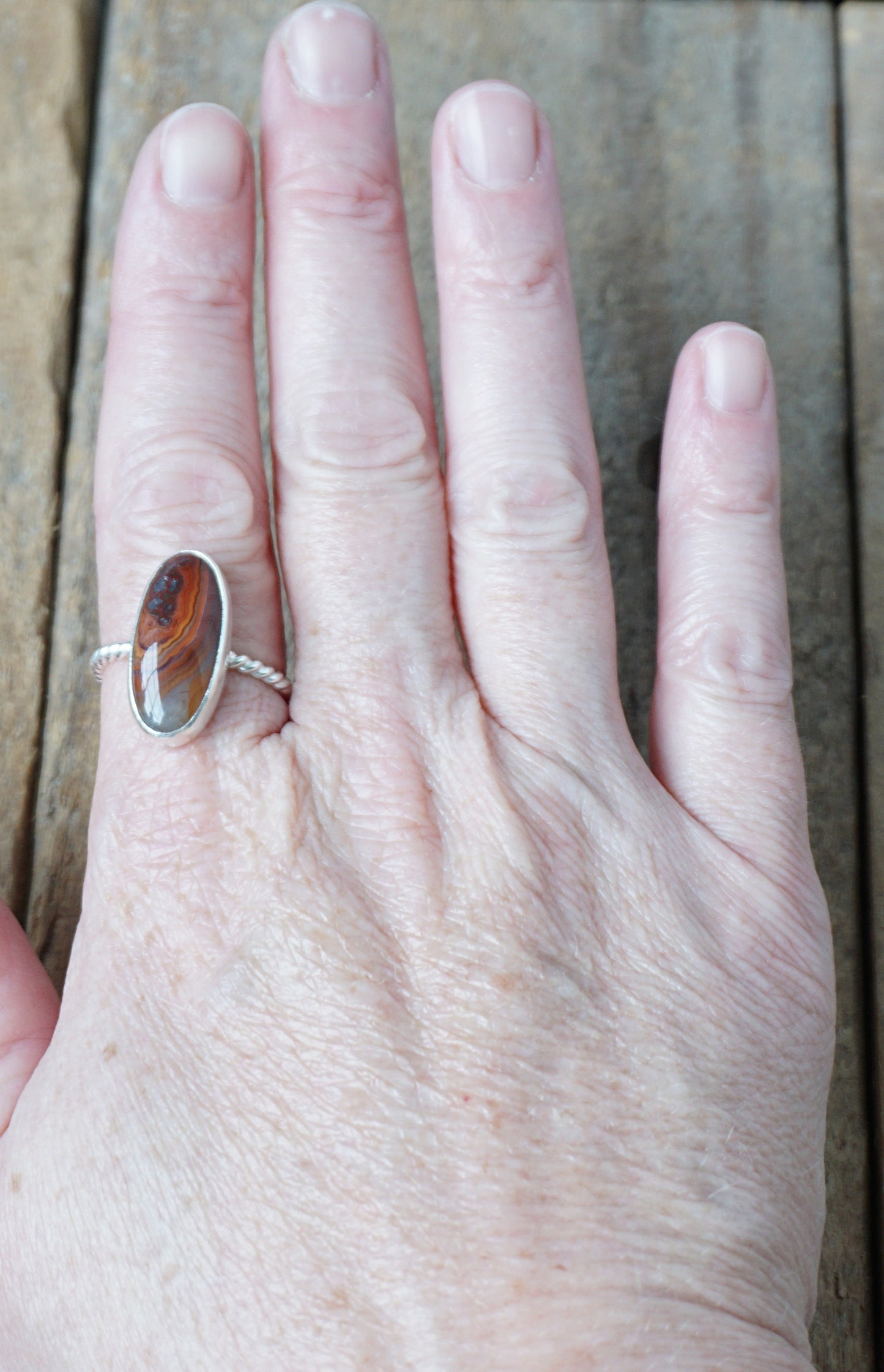 hand wearing a Silver ring with a brown oval stone on a wooden background
