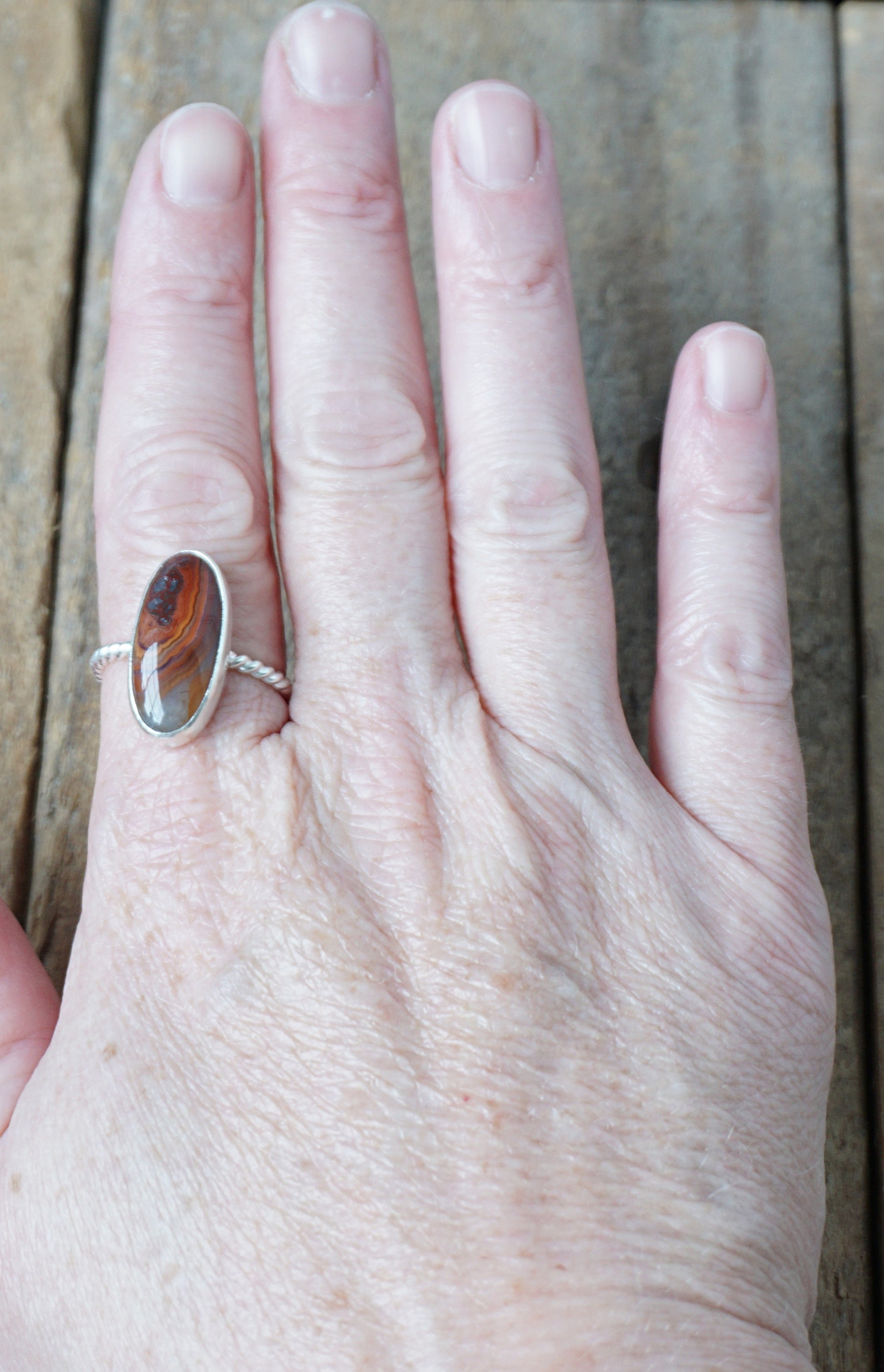 hand wearing a Silver ring with a brown oval stone on a wooden background