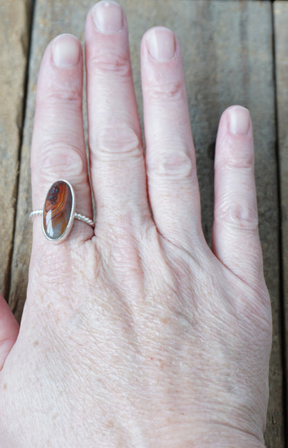 hand wearing a Silver ring with a brown oval stone on a wooden background
