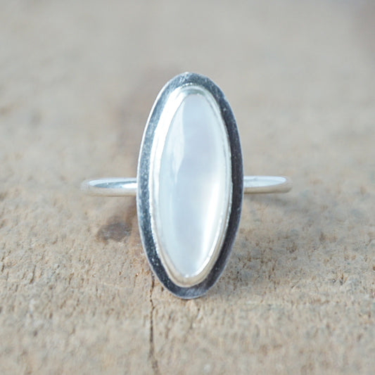 Silver ring with a white stone on a wooden surface