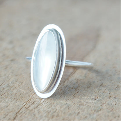 Silver ring with a white stone on a wooden surface