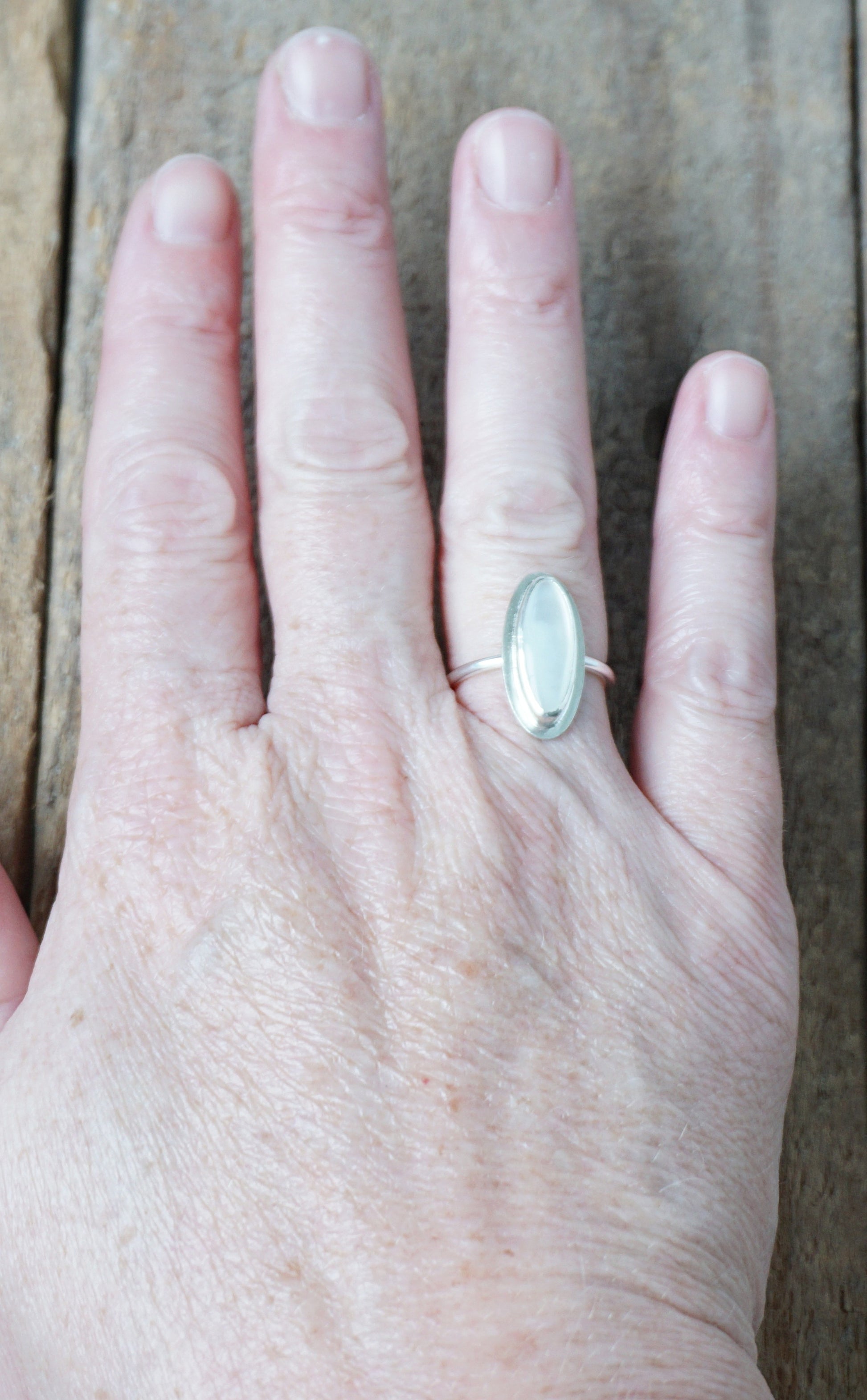 Hand wearing a silver ring with a white stone, on a wooden surface
