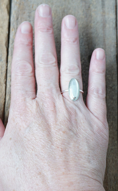 Hand wearing a silver ring with a white stone, on a wooden surface
