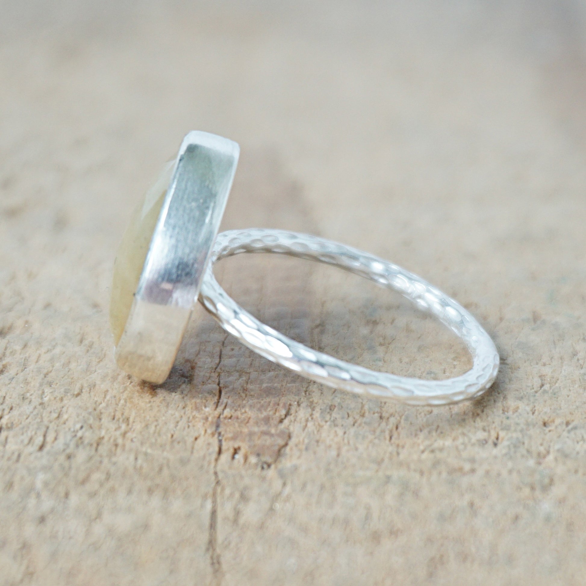 side view of a silver ring with a tan stone on a wooden background