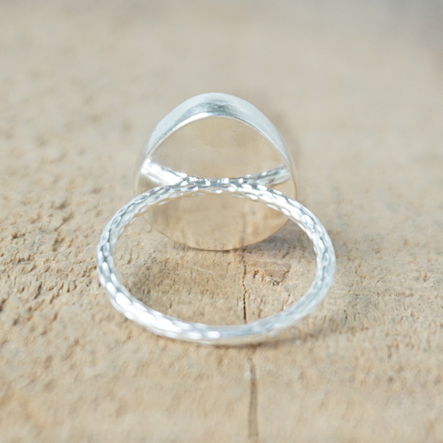 back view of a silver ring with a tan stone on a wooden background