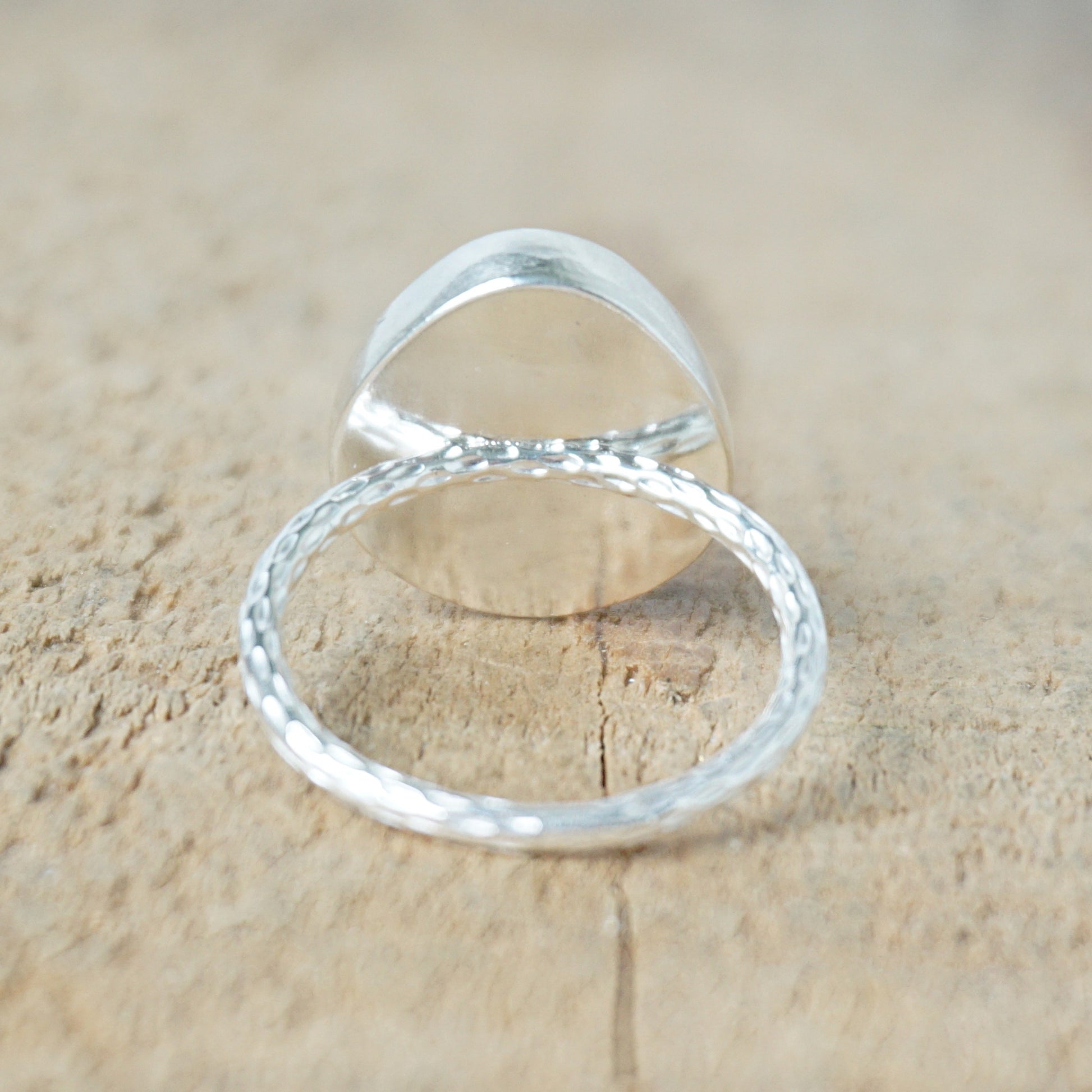 back view of a silver ring with a tan stone on a wooden background