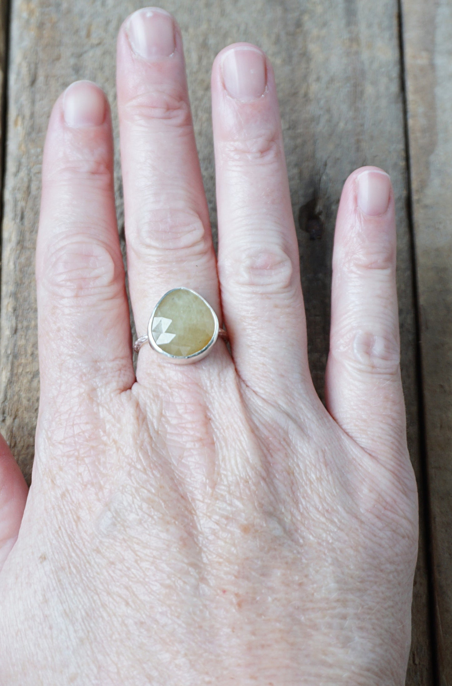 hand wearing a silver ring with a tan stone on a wooden background