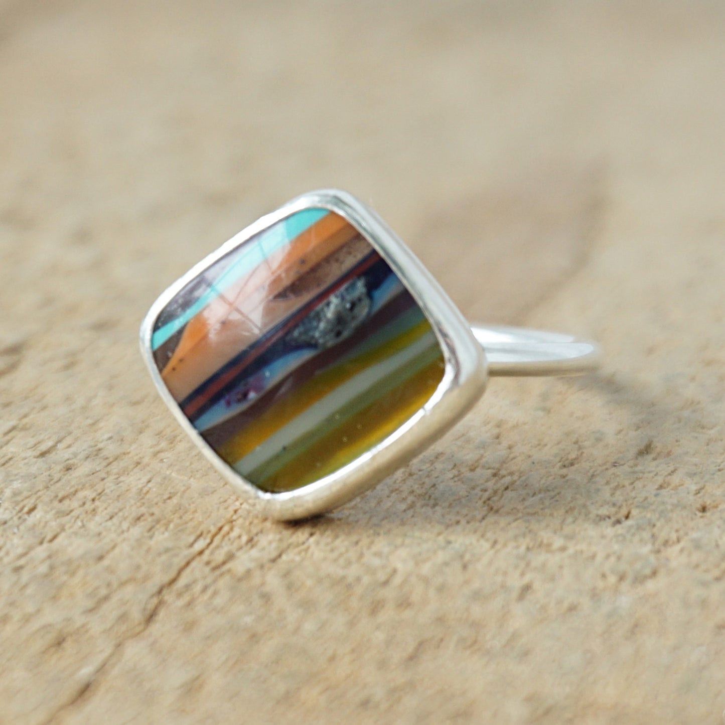 Silver ring with a colorful stone on a wooden surface