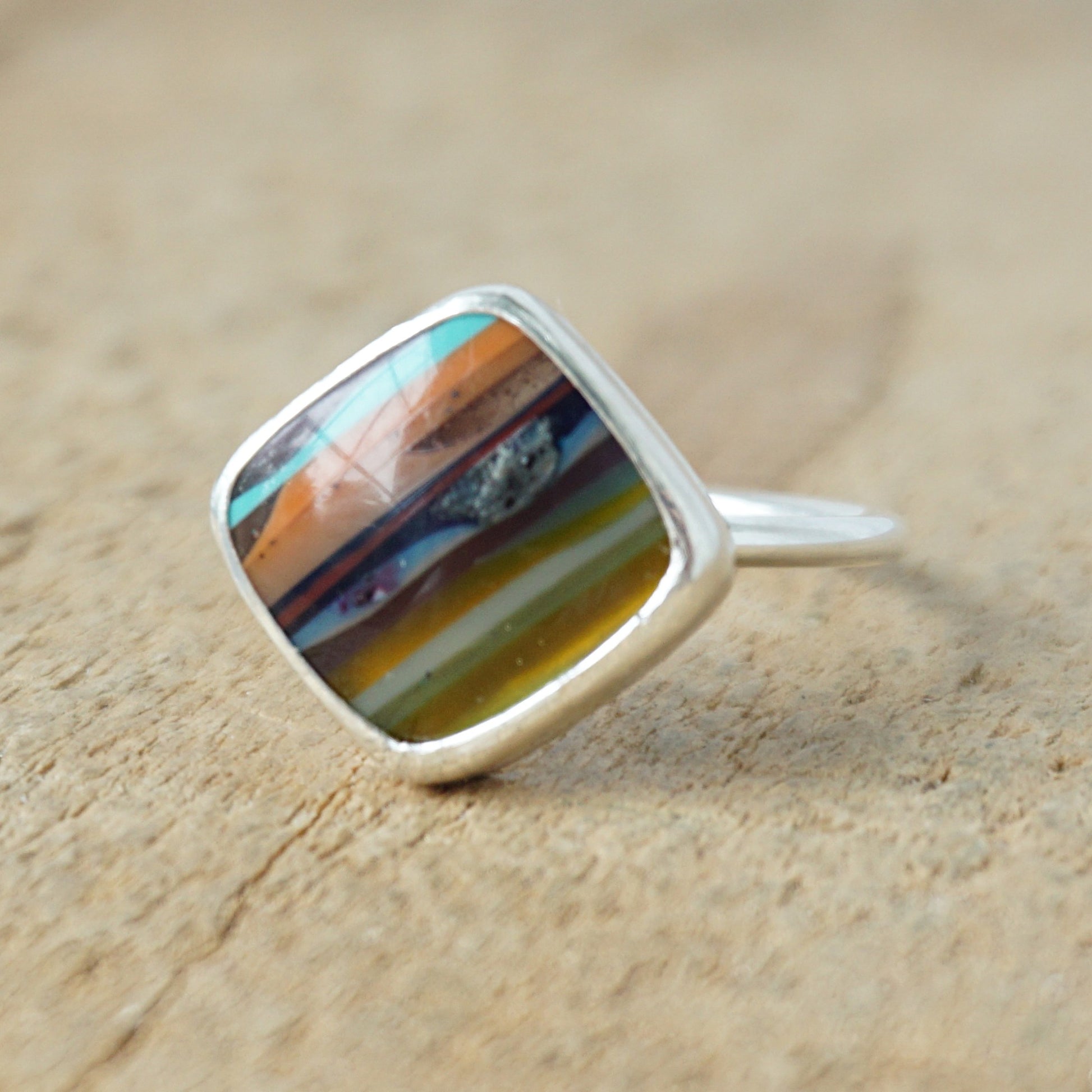 Silver ring with a colorful stone on a wooden surface