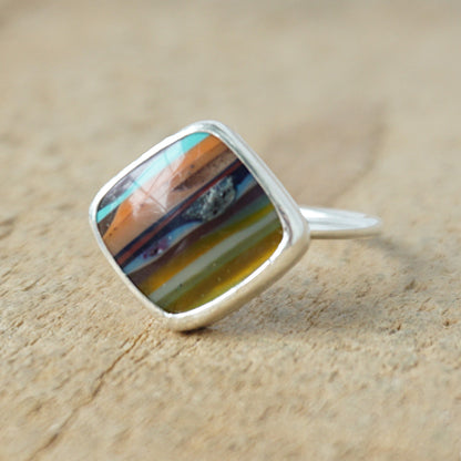 Silver ring with a colorful stone on a wooden surface