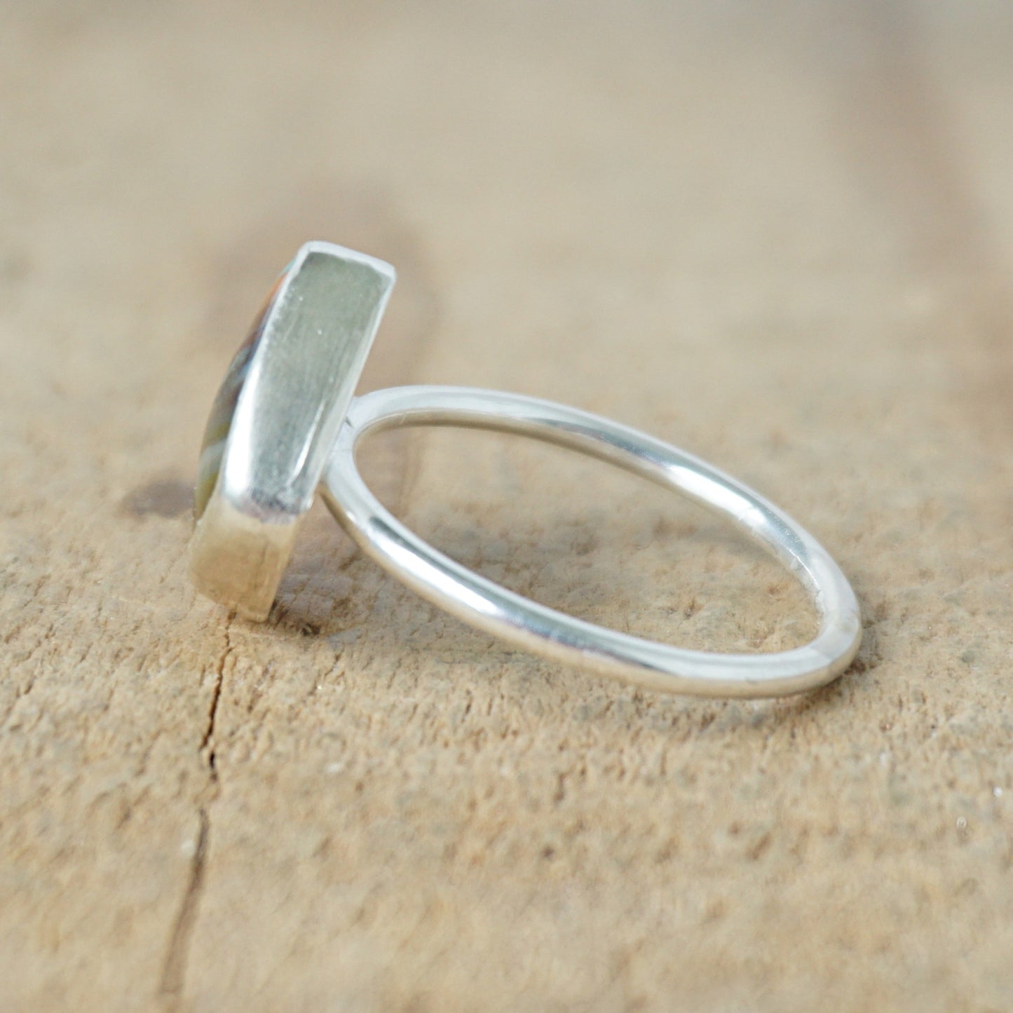 side view of a silver ring with a striped stone on a wooden background