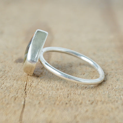 side view of a silver ring with a striped stone on a wooden background