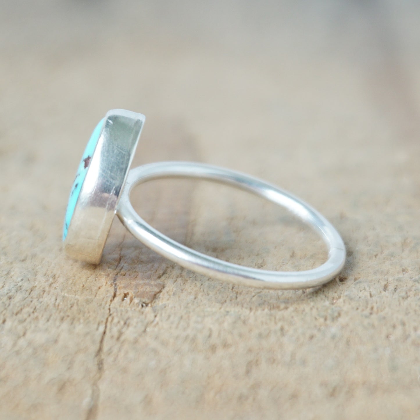 side view of a Turquoise ring with silver band on a wooden surface