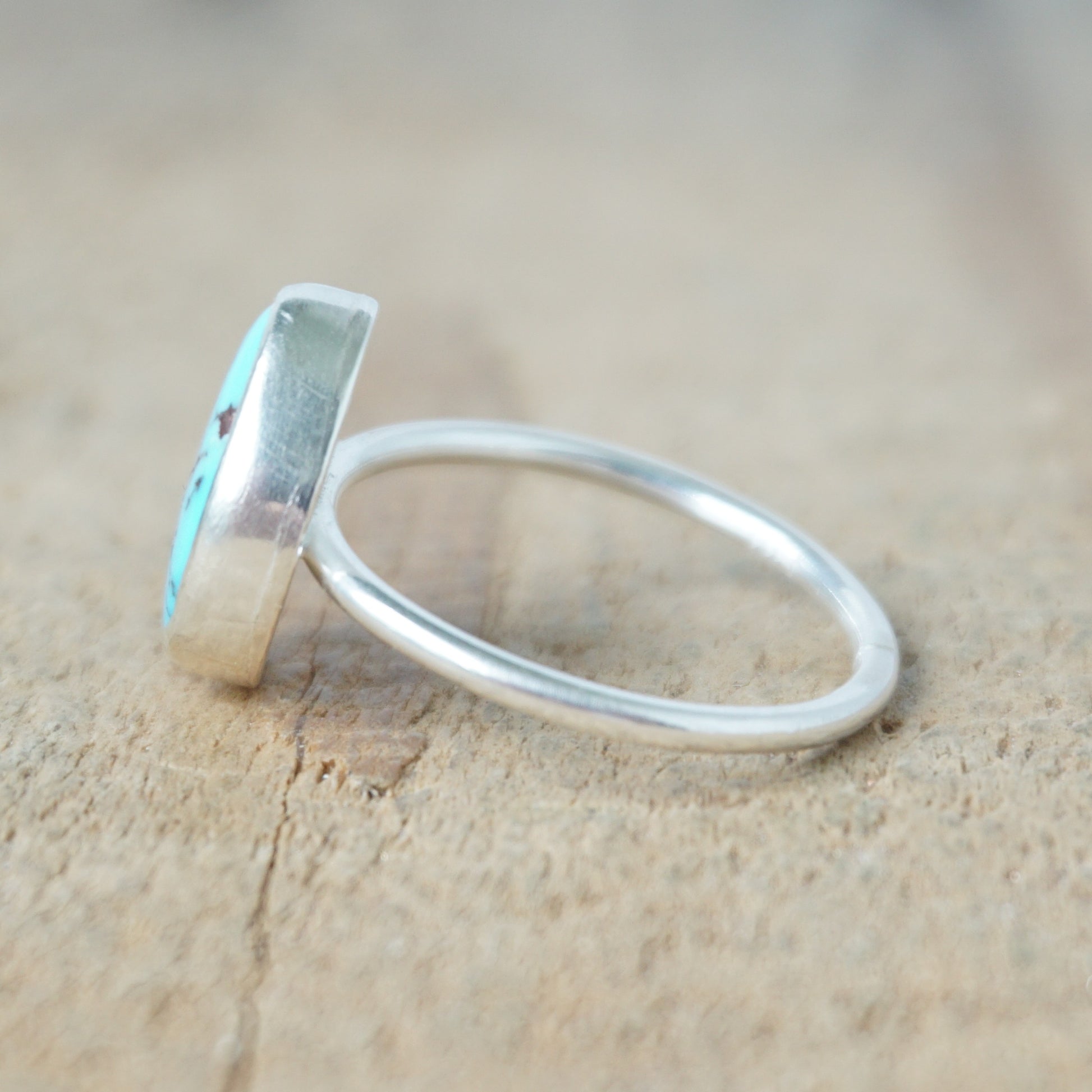 side view of a Turquoise ring with silver band on a wooden surface