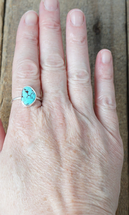 Hand wearing a turquoise ring on a wooden surface