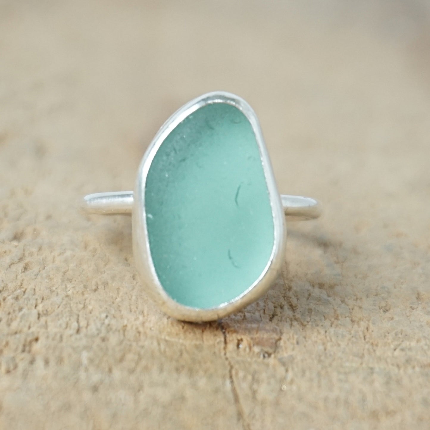 teal sea glass ring with a sterling silver setting, against a wooden background