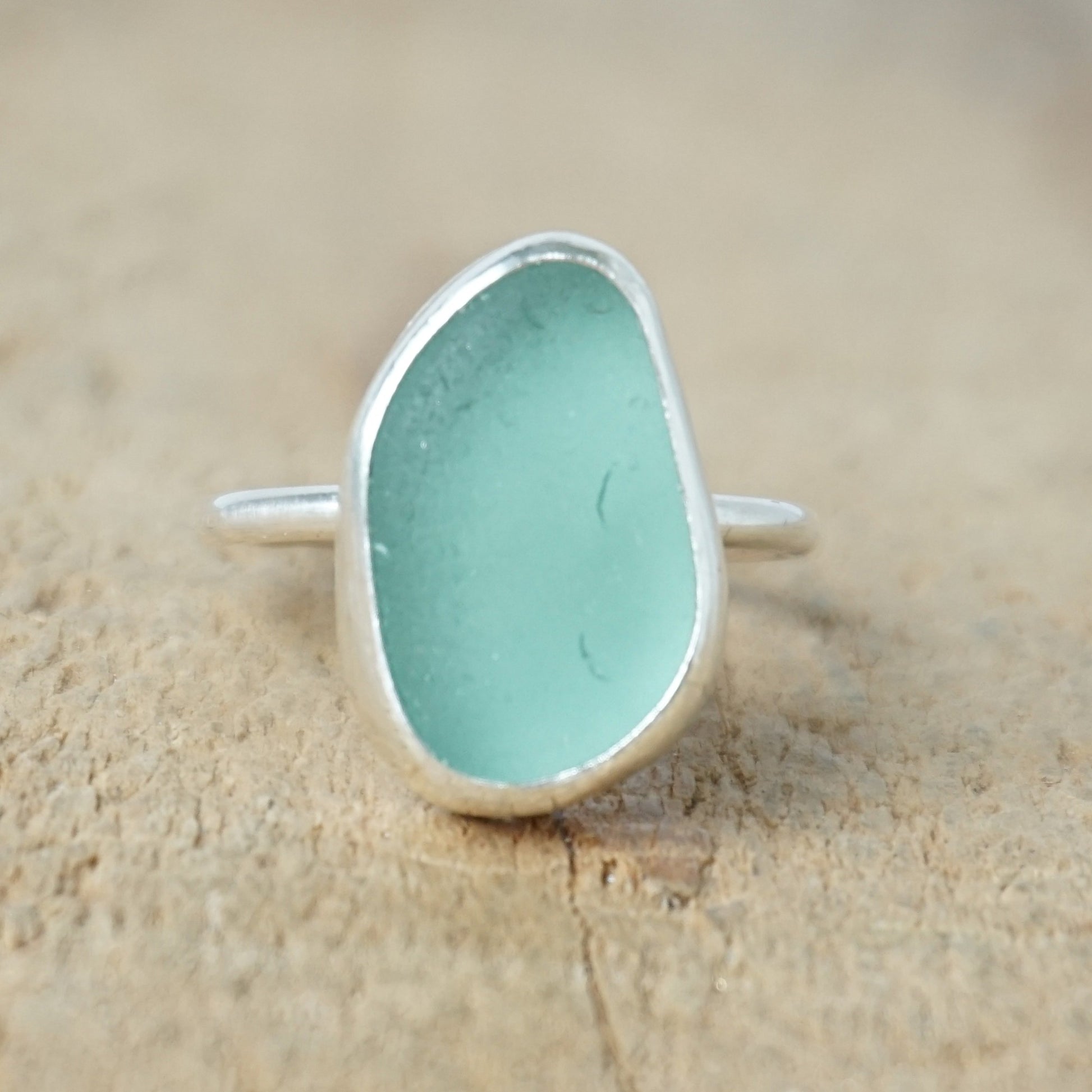 teal sea glass ring with a sterling silver setting, against a wooden background