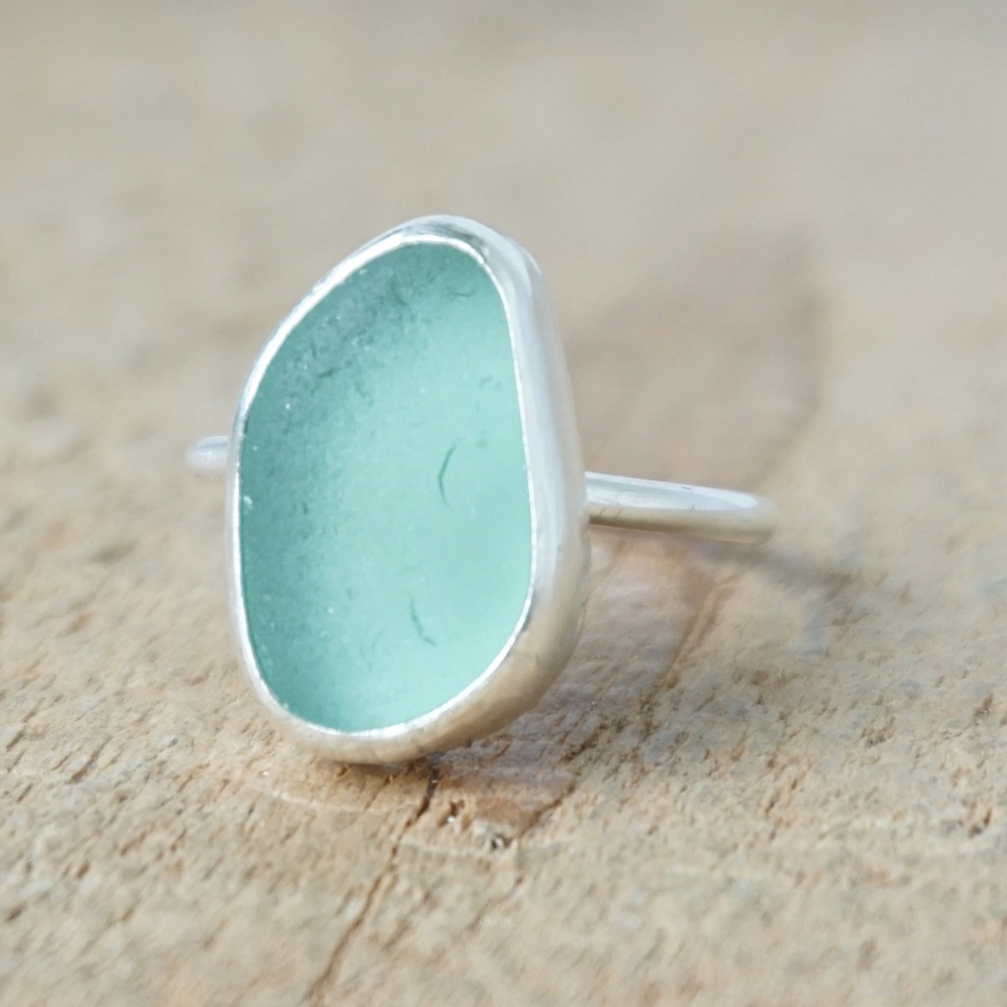 teal sea glass ring with a sterling silver setting, against a wooden background