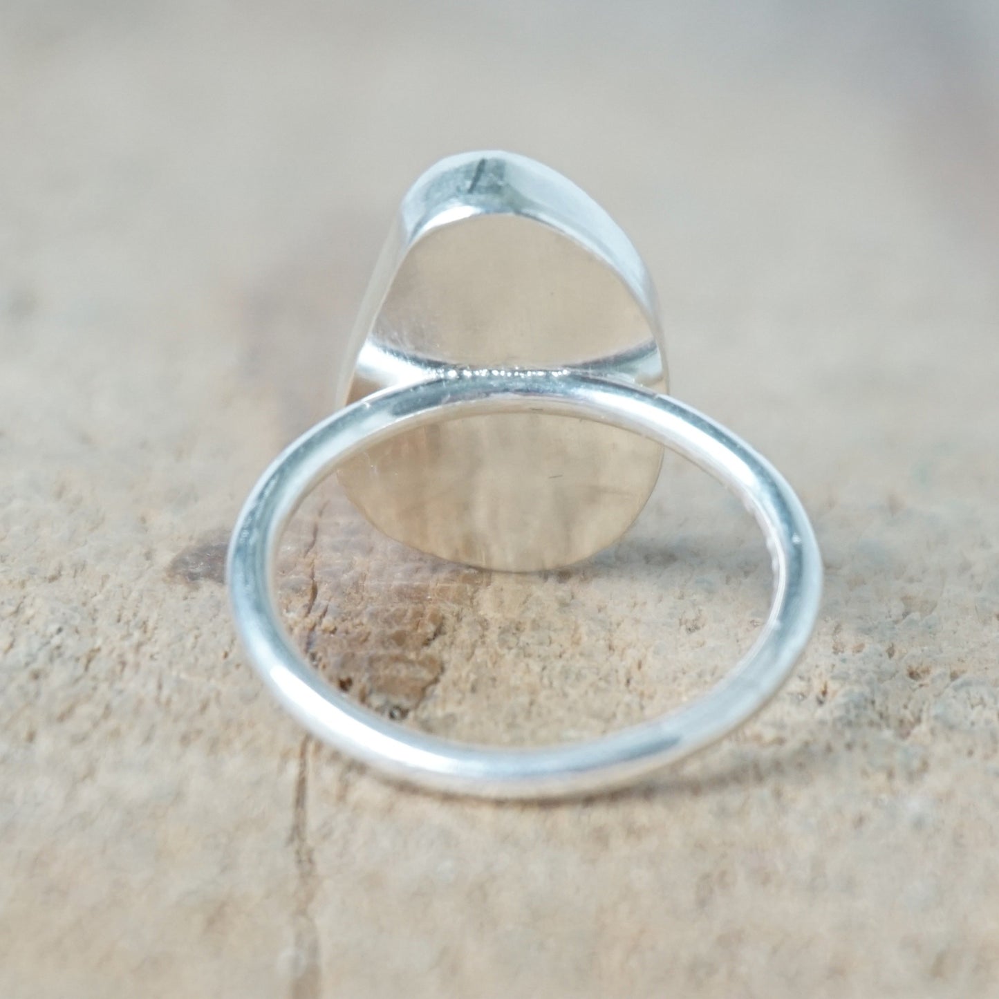 back view of a teal sea glass ring with a sterling silver setting, against a wooden background
