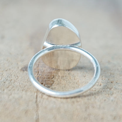 back view of a teal sea glass ring with a sterling silver setting, against a wooden background