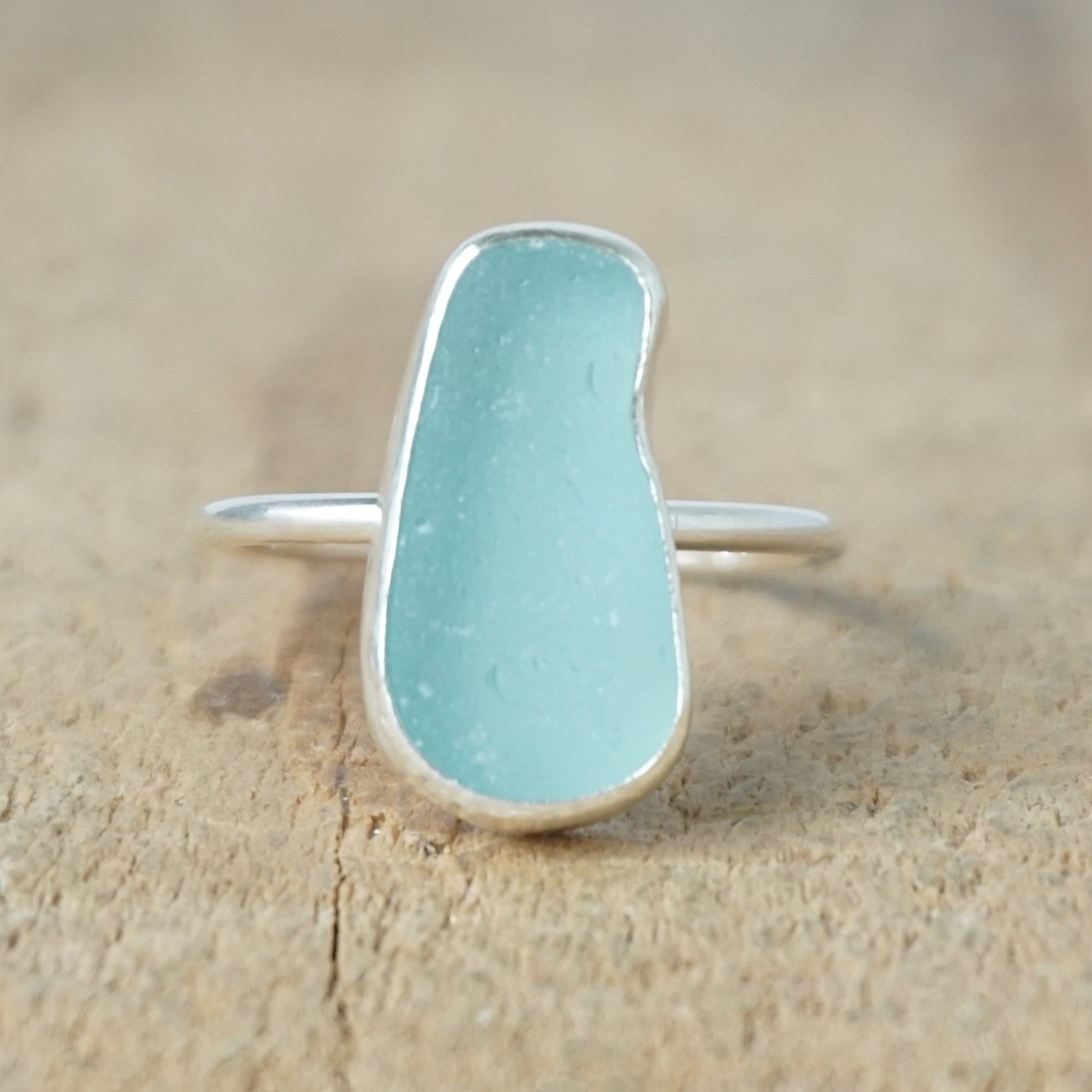 teal sea glass ring with a sterling silver setting, against a wooden background