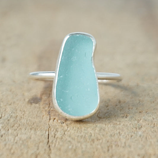 teal sea glass ring with a sterling silver setting, against a wooden background
