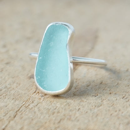 teal sea glass ring with a sterling silver setting, against a wooden background