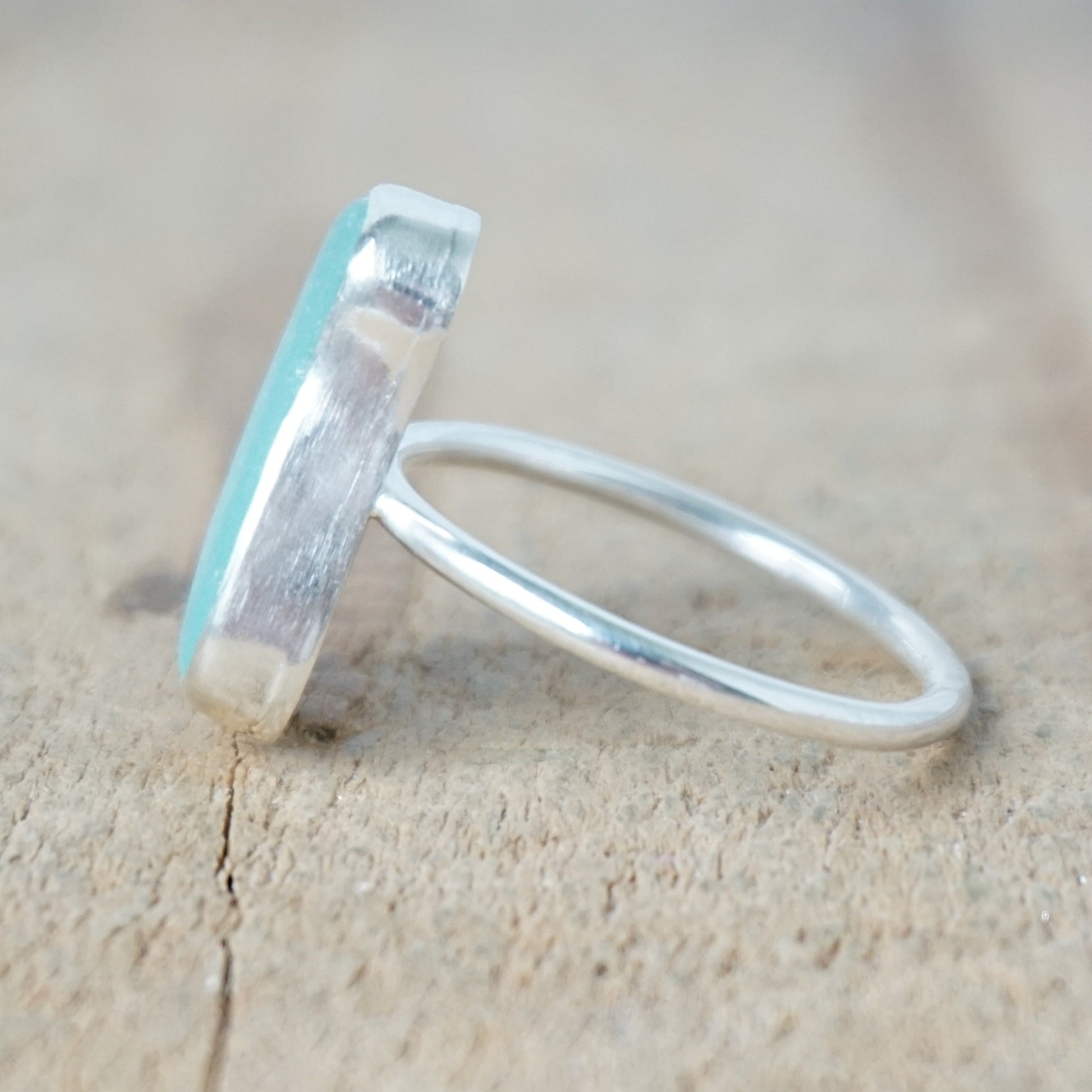 side view of a teal sea glass ring with a sterling silver setting, against a wooden background