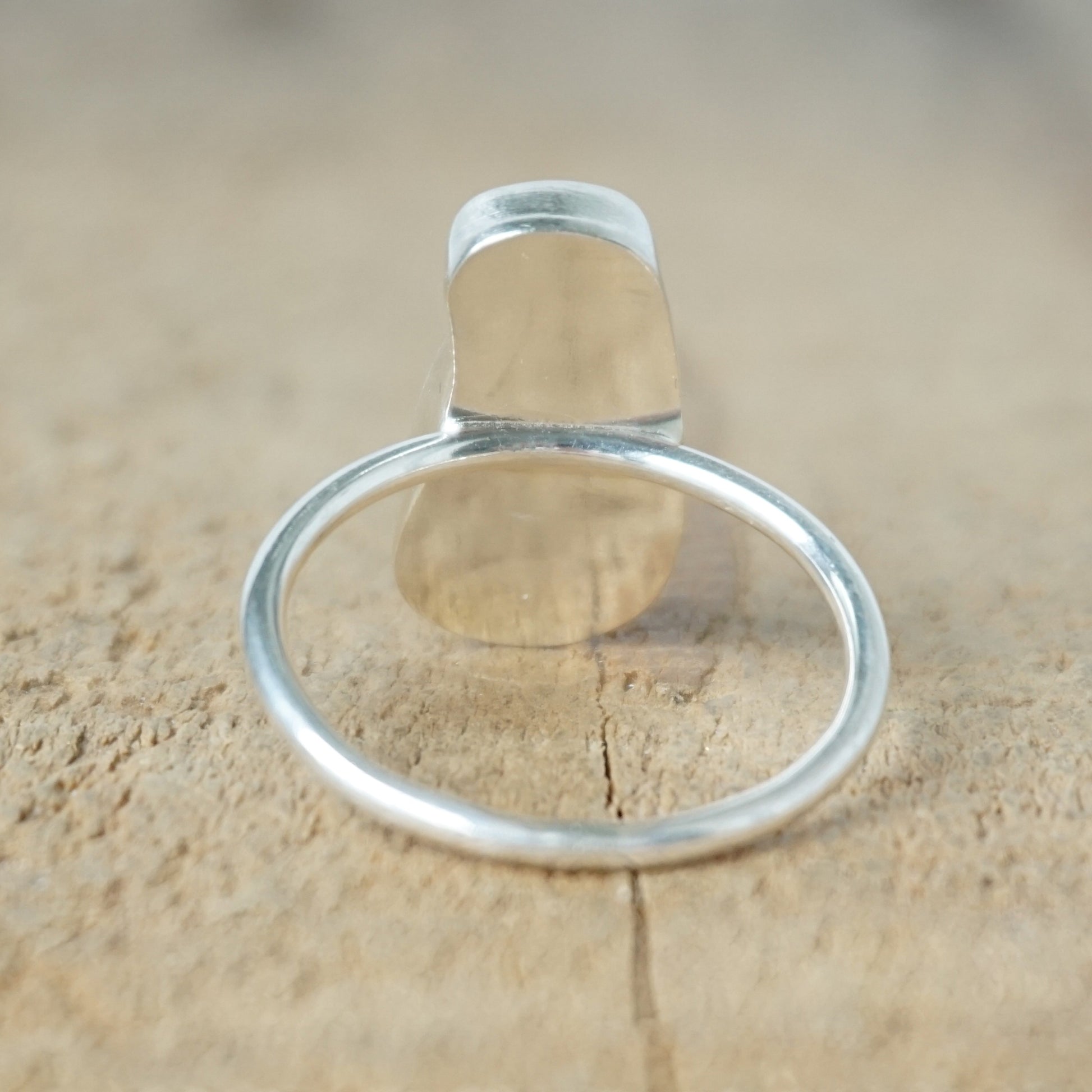 back view of a teal sea glass ring with a sterling silver setting, against a wooden background