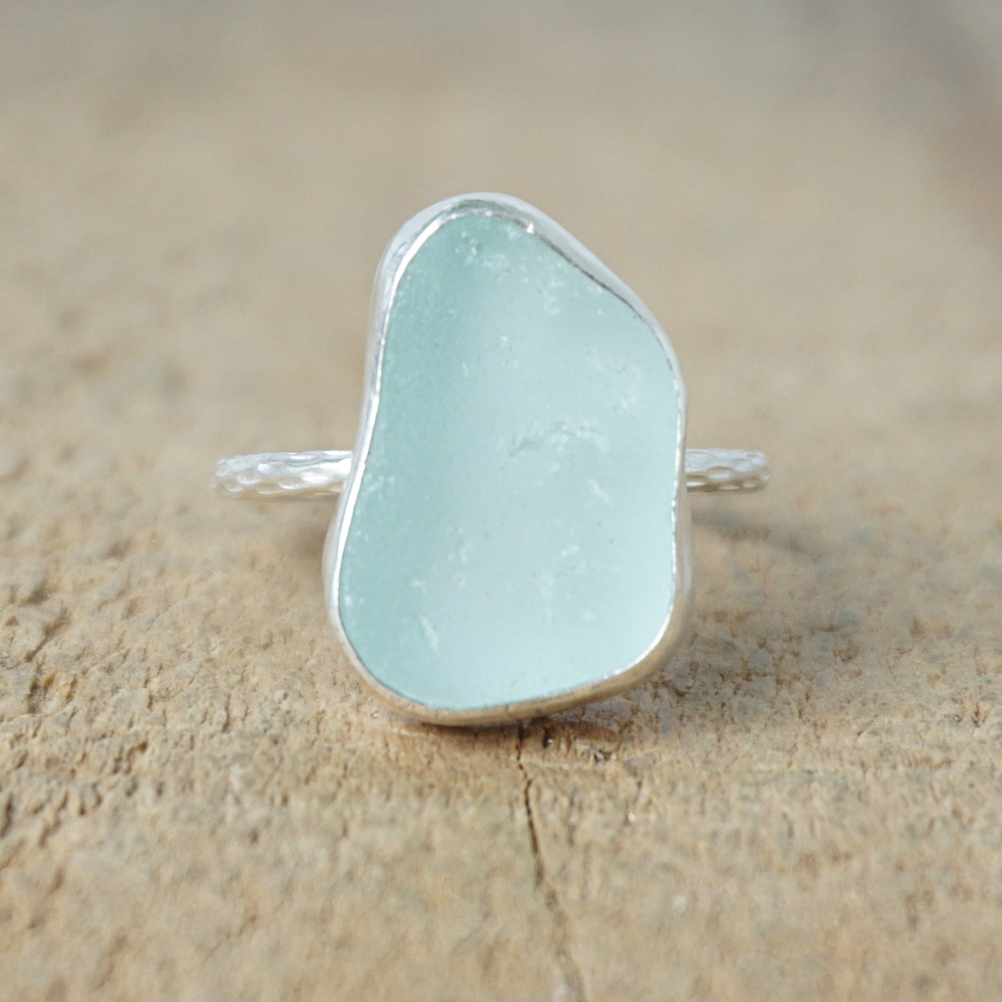 light aqua blue sea glass ring with a sterling silver setting, against a wooden background