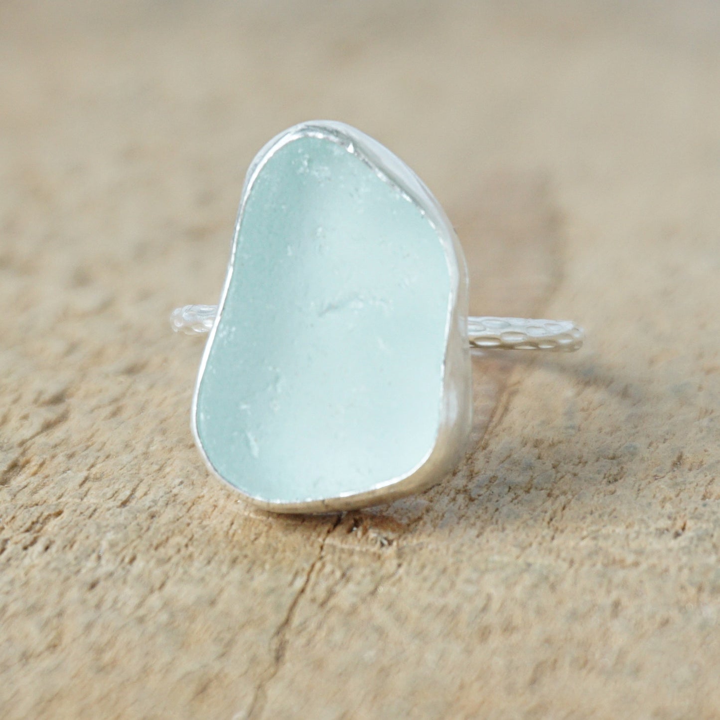 light aqua blue sea glass ring with a sterling silver setting, against a wooden background