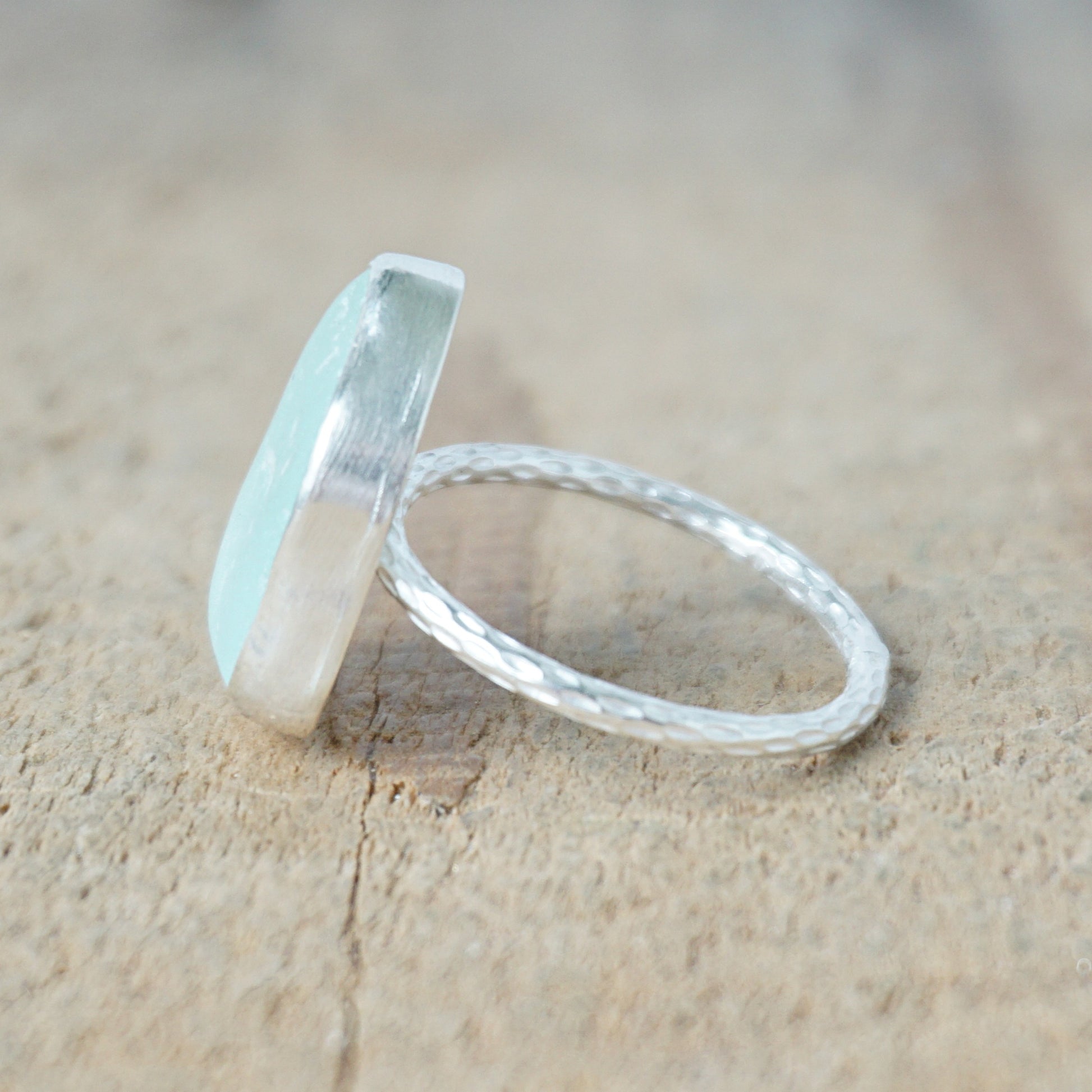 side view of a light aqua blue sea glass ring with a sterling silver setting, against a wooden background