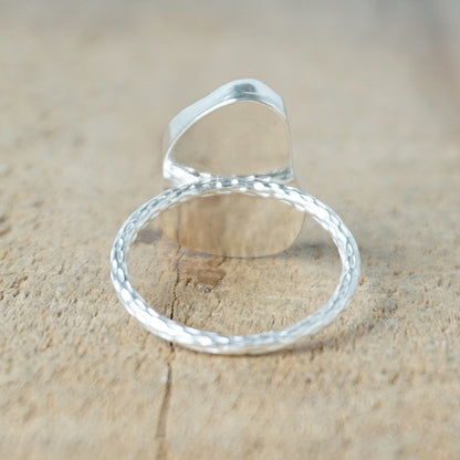 back view of a light aqua blue sea glass ring with a sterling silver setting, against a wooden background