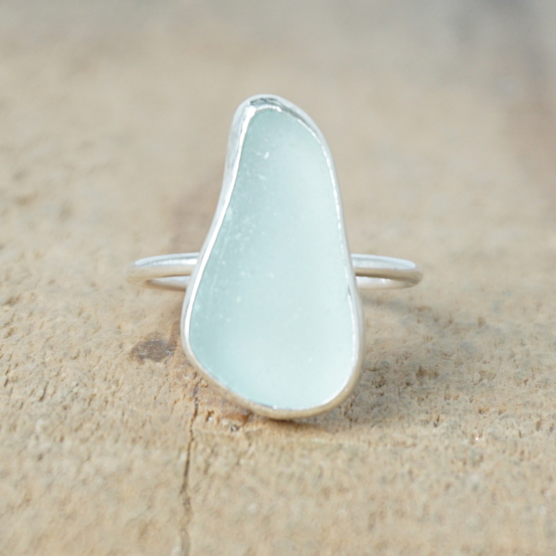 light aqua blue sea glass ring with a sterling silver setting, against a wooden background