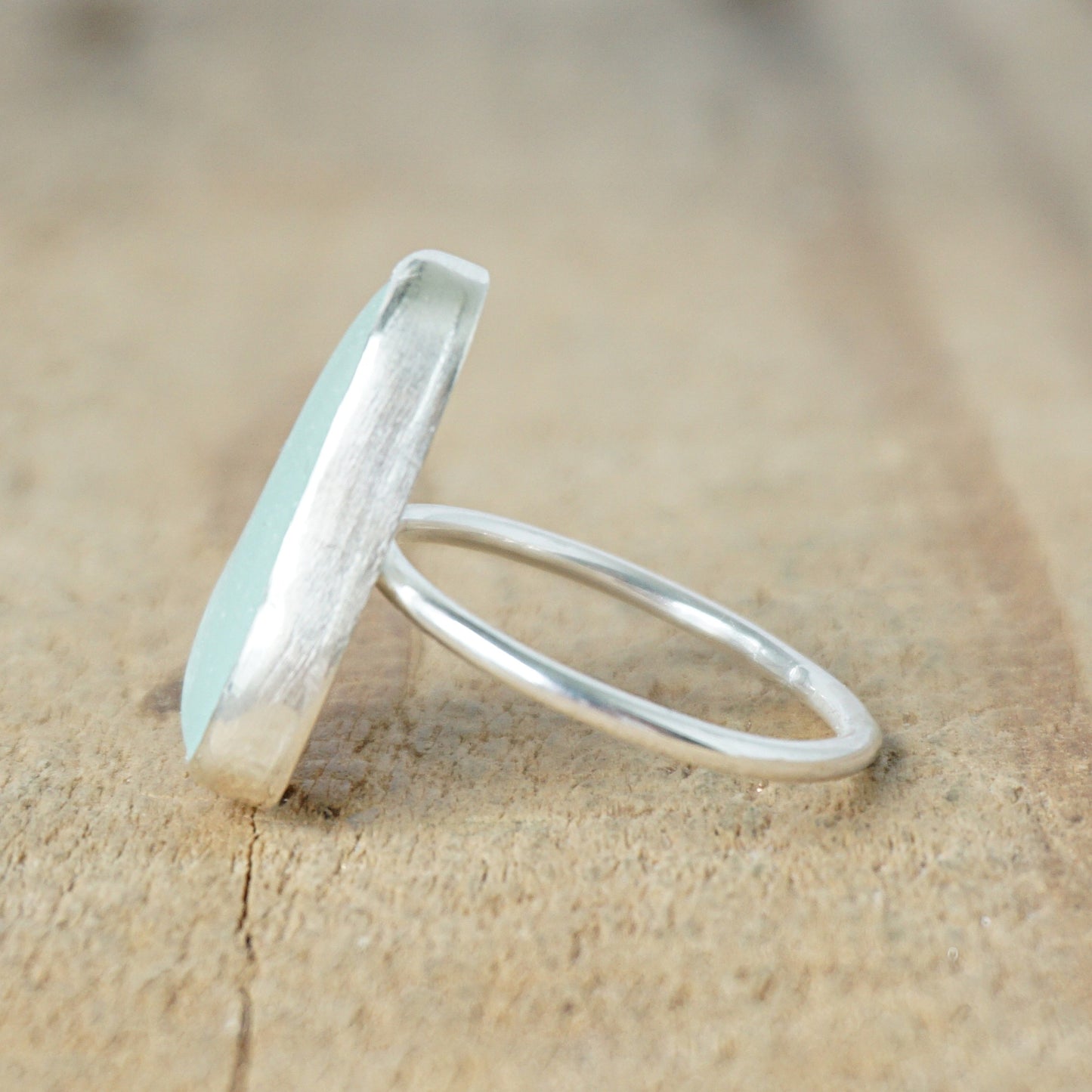 side view of a light aqua blue sea glass ring with a sterling silver setting, against a wooden background