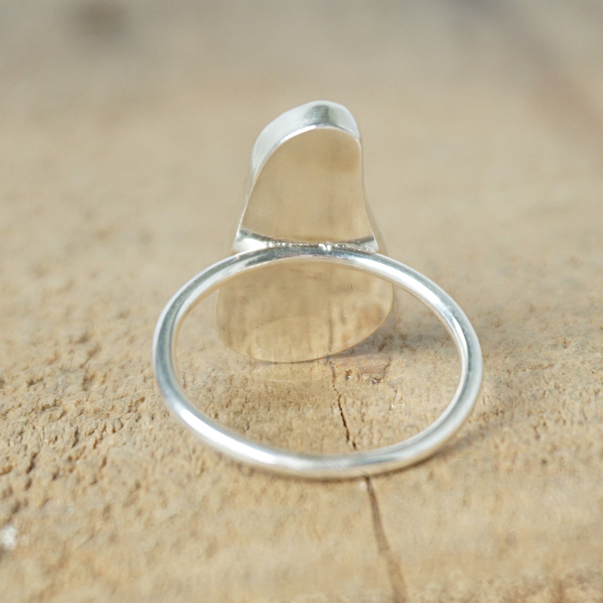 back view of a light aqua blue sea glass ring with a sterling silver setting, against a wooden background