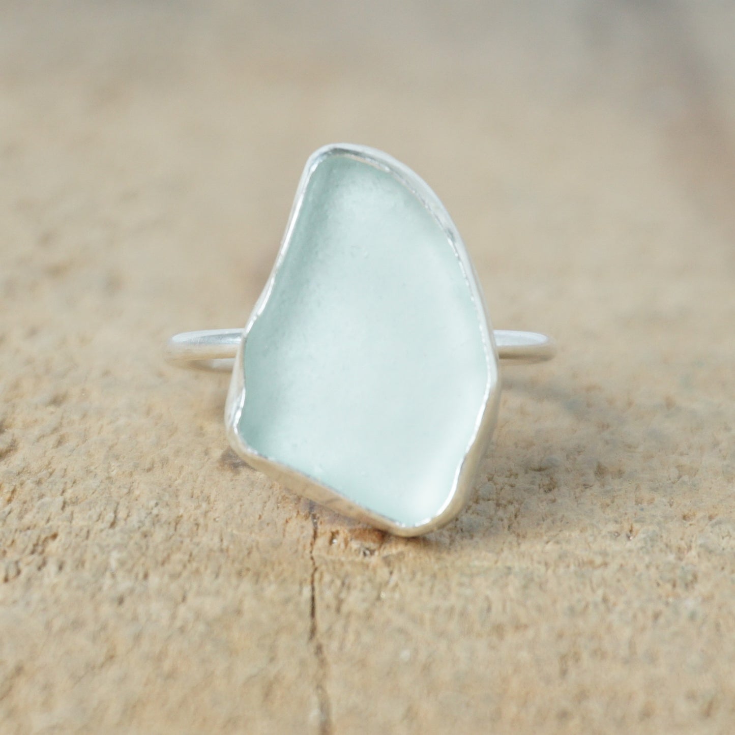 light aqua blue sea glass ring with a sterling silver setting, against a wooden background